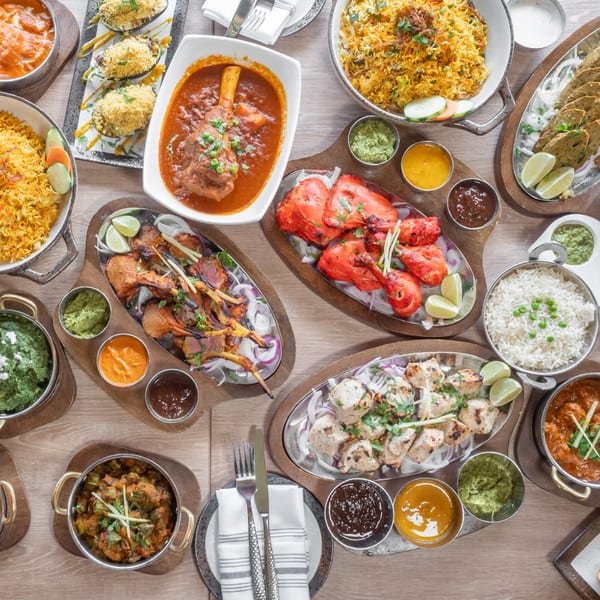 An overhead view of a large spread of various Indian dishes, including curries, rice, and grilled meats.