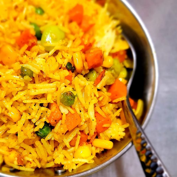 Close-up of vibrant Indian vegetable biryani with rice, peas, carrots, and corn in a metal bowl.