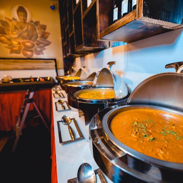 A buffet line of Indian dishes in chafing dishes, with a Buddha mural in the background.