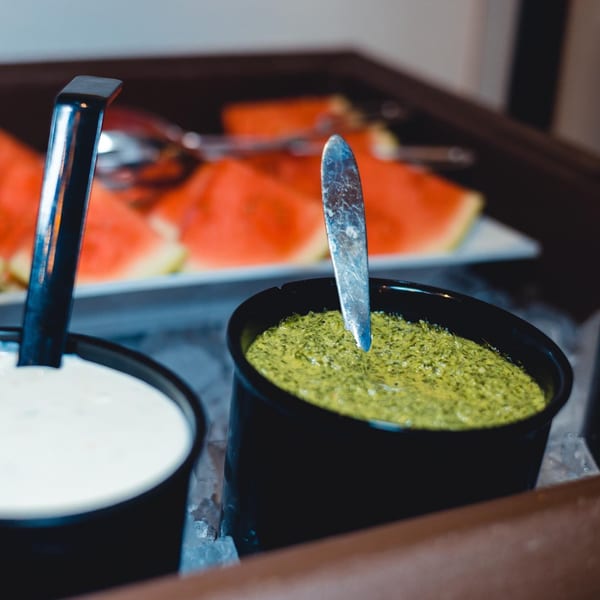 Two bowls of Indian sauces, one green and one white, with watermelon slices in the background.