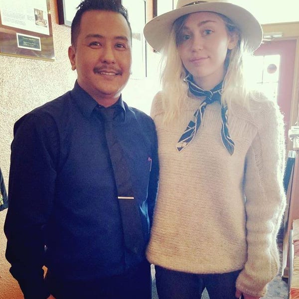 A man in a black shirt and tie stands next to a woman in a hat and sweater.
