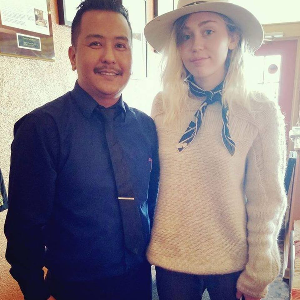 A man in a black shirt and tie stands next to a woman in a hat and sweater.