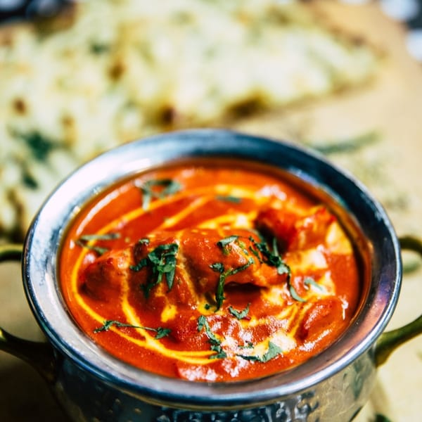 A close-up of Namaste India Bistro's butter chicken, garnished with cream and cilantro, with naan in the background.